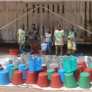 Fünf Personen stehen vor einer Holzwand und vor ihnen sind Eimer aufgereiht 