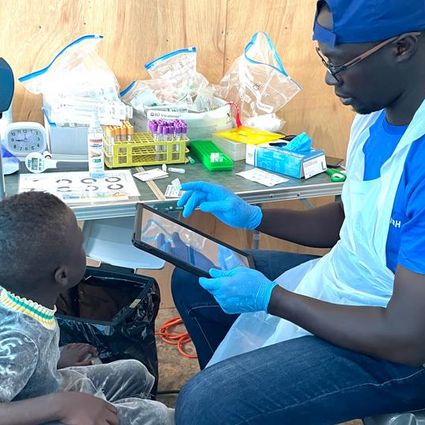 Healthcare worker examines a child using a tablet in the temporary study clinic