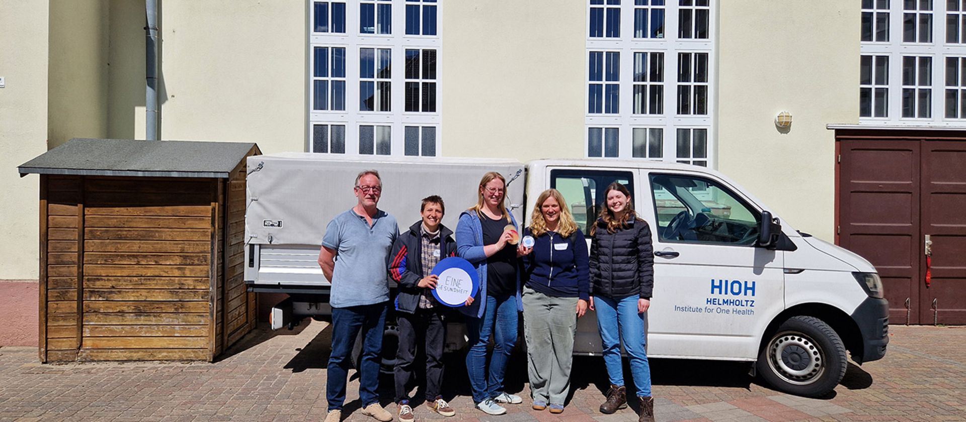Gruppenbild vor einem Auto und Gebäude draußen