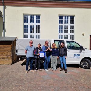 Gruppenbild vor einem Auto und Gebäude draußen